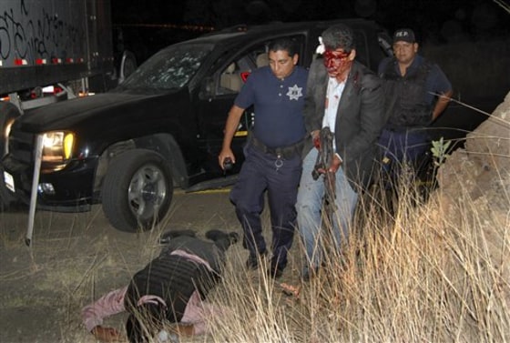 An injured bodyguard of Mexico's Michoacan state's public safety secretary walks with help from a police officer after being wounded during a shootout in Morelia, Mexico, early Saturday. A fellow bodyguard lies dead. 
